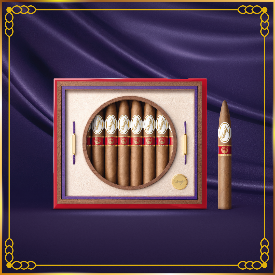 A premium Davidoff Year of the Sheep 2027 cigar box displayed on a deep purple satin background with a gold decorative border. The set includes a red and purple presentation box with a circular window showing cigars with white and red bands, alongside a single upright cigar.