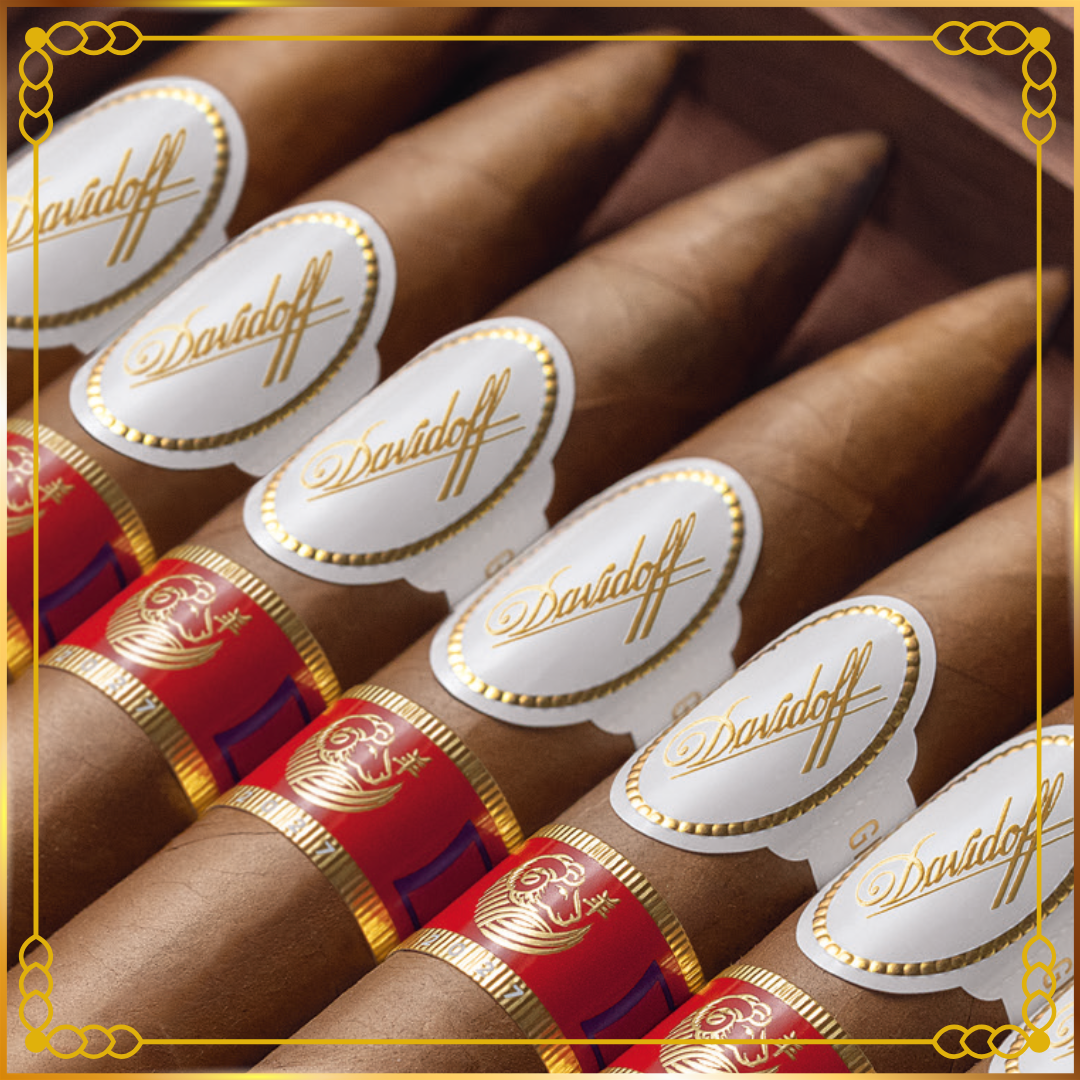 A close-up of several Davidoff Year of the Sheep 2027 cigars arranged diagonally, each with a white oval Davidoff label and a red band with gold detailing. The cigars are brown, and the background is a dark brown wooden box.