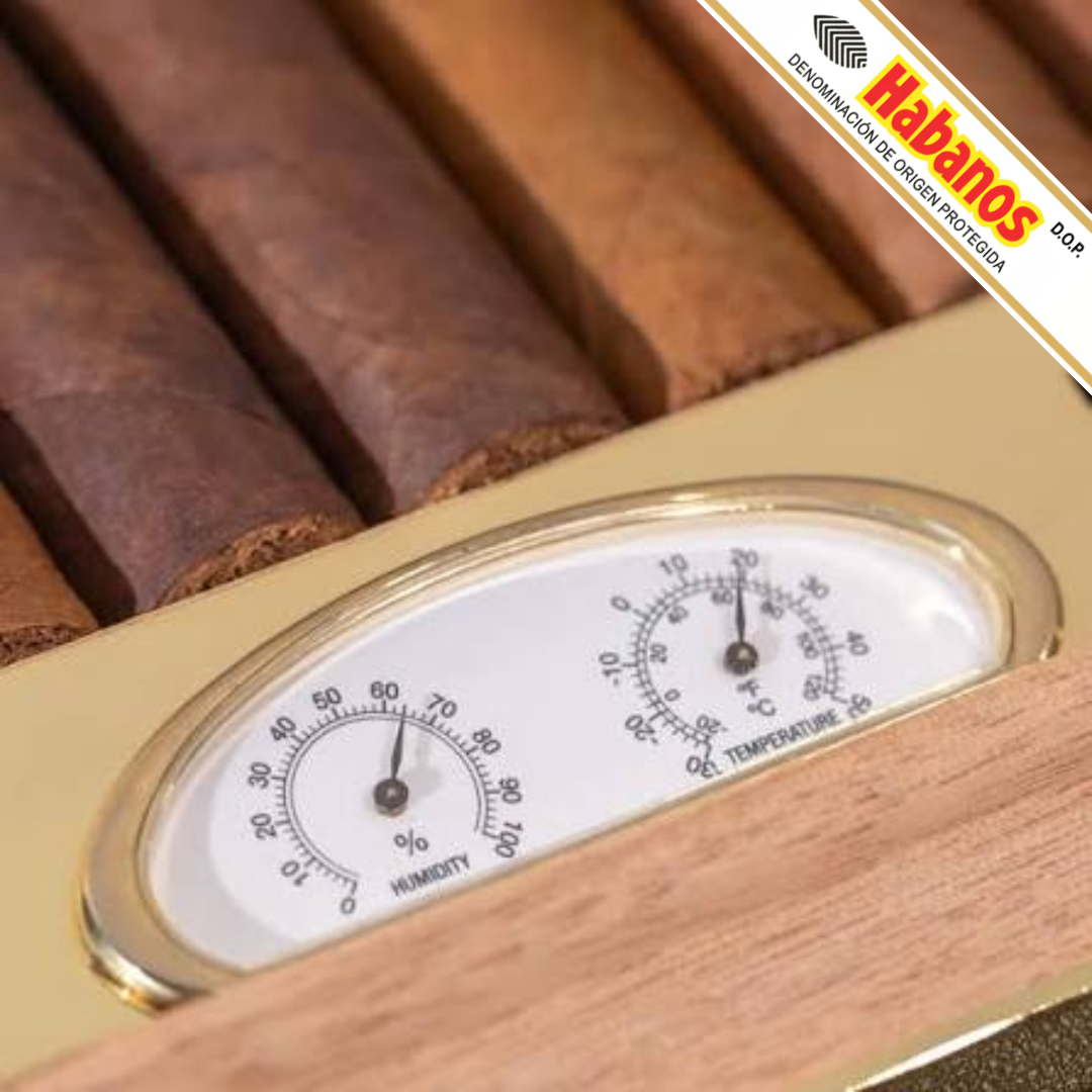 Close-up of a Cohiba Selección 50th Anniversary Travel Humidor with a brass-and-wood humidifier gauge, showing cigars inside and a Habanos diagonal brand overlay in the top-right corner.