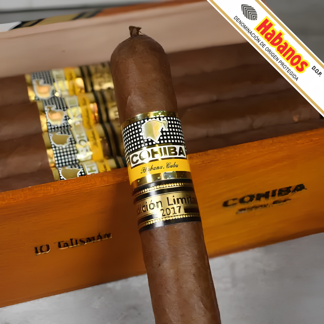 A single Cohiba Talisman Limited Edition 2017 cigar with a yellow and black band stands upright in front of an open wooden cigar box. The box is branded COHIBA and contains wrapped cigars.
