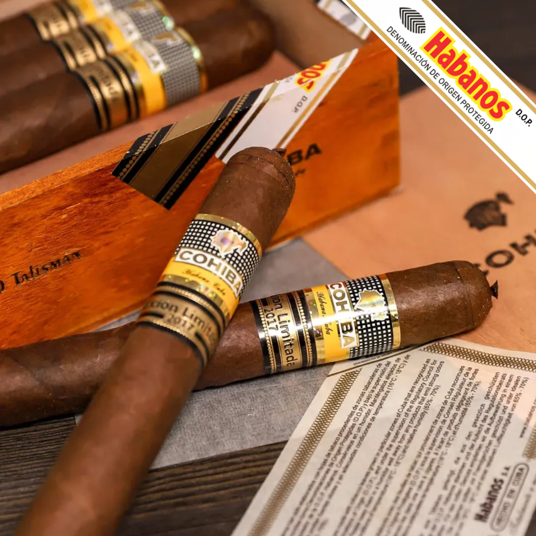 Close-up of several Cohiba Talisman Limited Edition 2017 cigars arranged on a wooden surface with branded paper and a wooden cigar box. The cigars have brown wrappers and yellow-and-black bands, with the Habanos branding clearly visible.